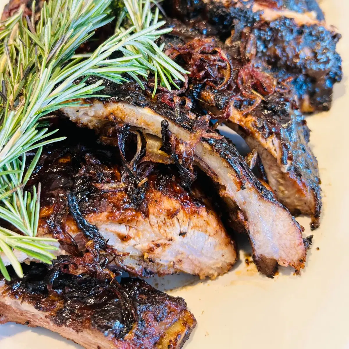 Sliced roasted lamb with a charred crust on a cream plate, fresh rosemary alongside
