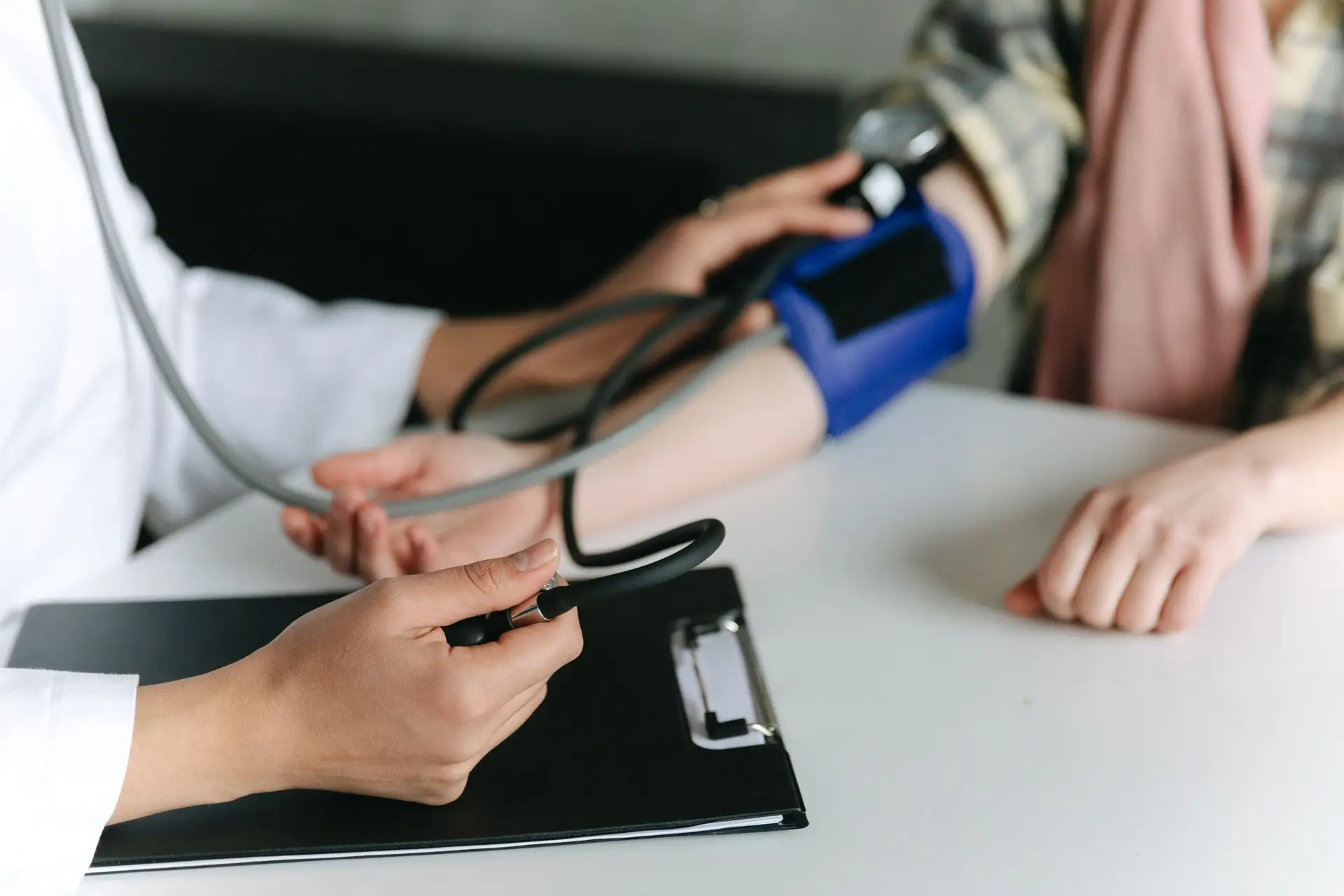A clinician taking a seated person's blood pressure with a cuff and stethoscope, both cropped at the shoulders